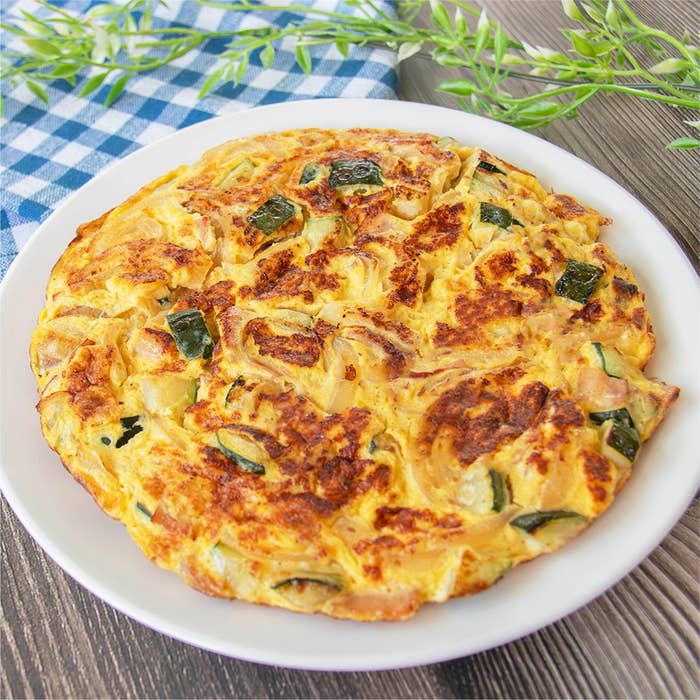 おいしそうなズッキーニのスパニッシュオムレツが白い皿に盛られている。中には玉ねぎ、ベーコンなども入っている。