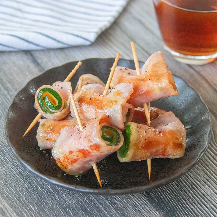 小皿にのったベーコンで巻かれたズッキーニの串、隣に飲み物が置かれている。