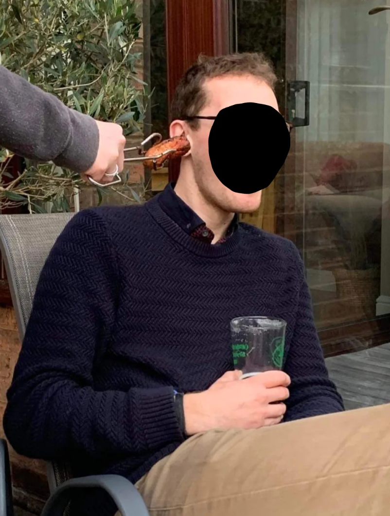 Person seated outdoors, holding a drink, portion    different  idiosyncratic  humorously presents a portion   of nutrient   adjacent   their caput  successful  a playful manner