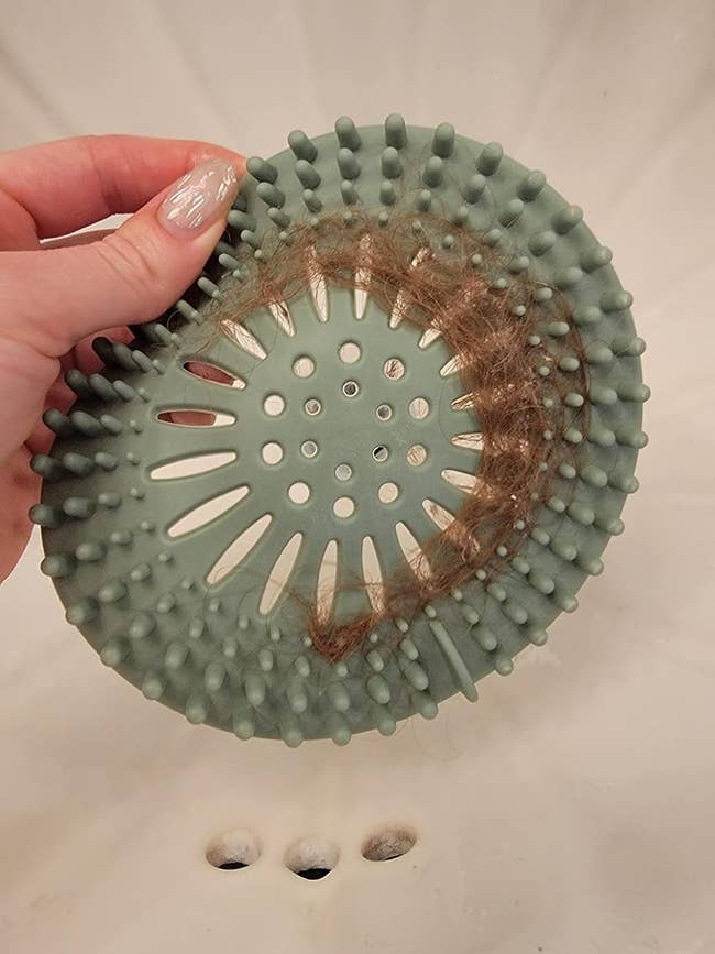 Hand holding a silicone drain hairsbreadth  catcher implicit    a sink, with hairsbreadth  caught successful  the catcher