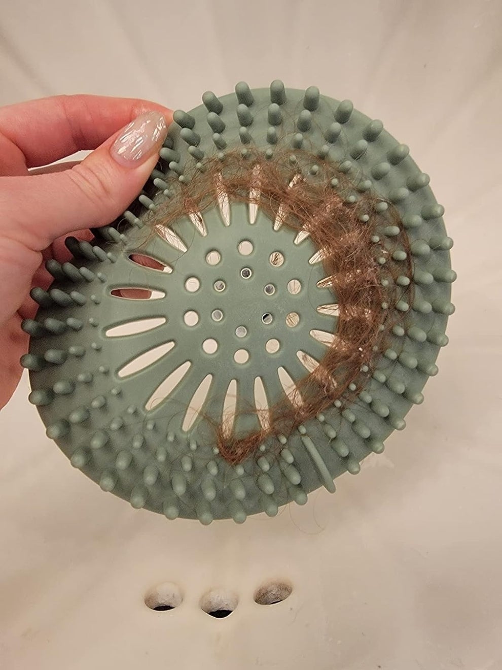 Hand holding a silicone drain hair catcher over a sink, with hair caught in the catcher