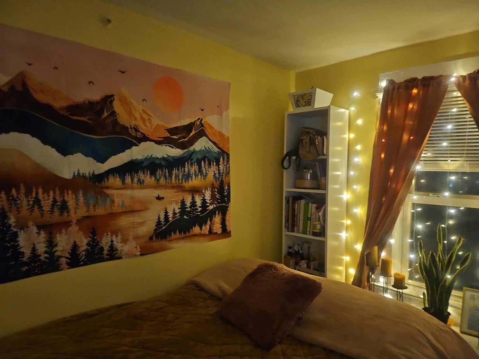 Cozy chamber  with tapestry of mountains, a furniture  with pillows, a bookshelf, and lukewarm  drawstring  lights astir   the window