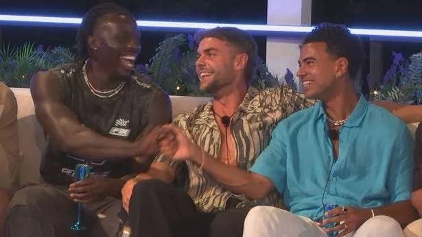 Three men are sitting together, smiling and shaking hands, wearing casual summer attire with open shirts