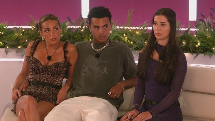 Three people seated on a couch during a TV show, wearing stylish leisure outfits and microphones