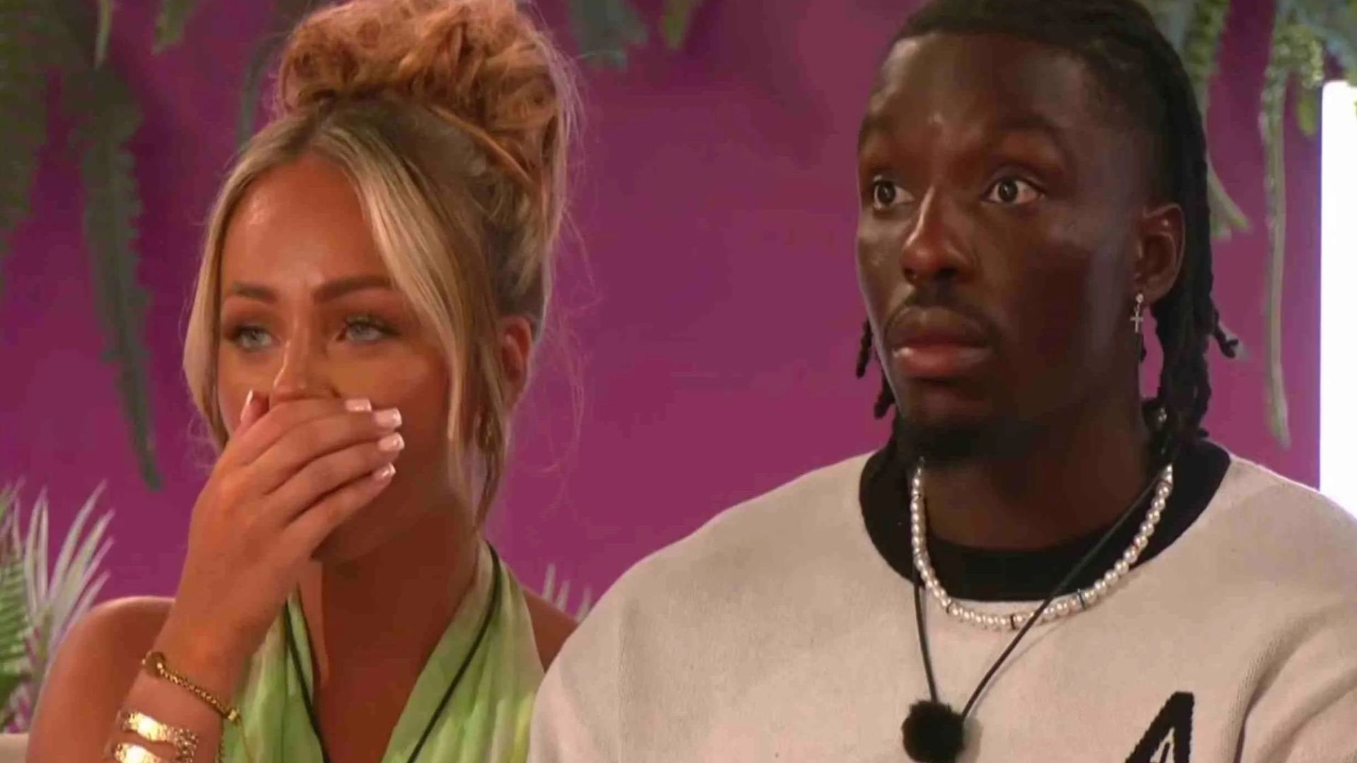 Two people looking surprised, one with a hand over their mouth, in a reality TV show setting