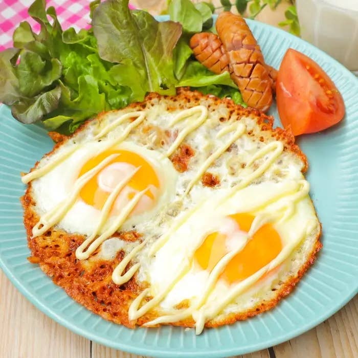 カリカリのチーズと一緒に焼いた目玉焼きにマヨネーズがかかっている。横にソーセージ、レタス、トマトが並んだ朝食プレート。