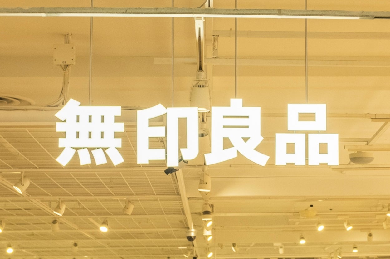 Store interior with shoppers and various household products on display. Signage with Japanese characters hangs from the ceiling