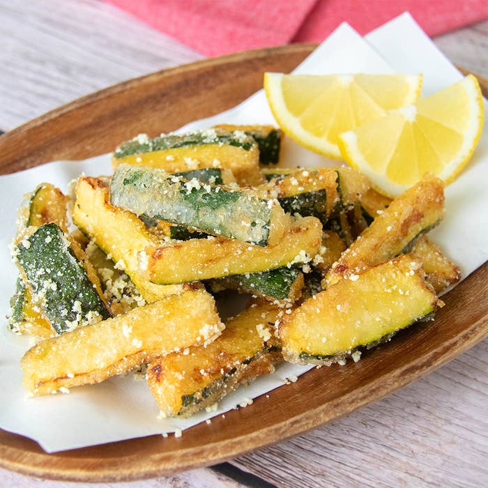 粉チーズと黒コショウがかかったズッキーニのフライとレモンのスライスが皿に盛られている。