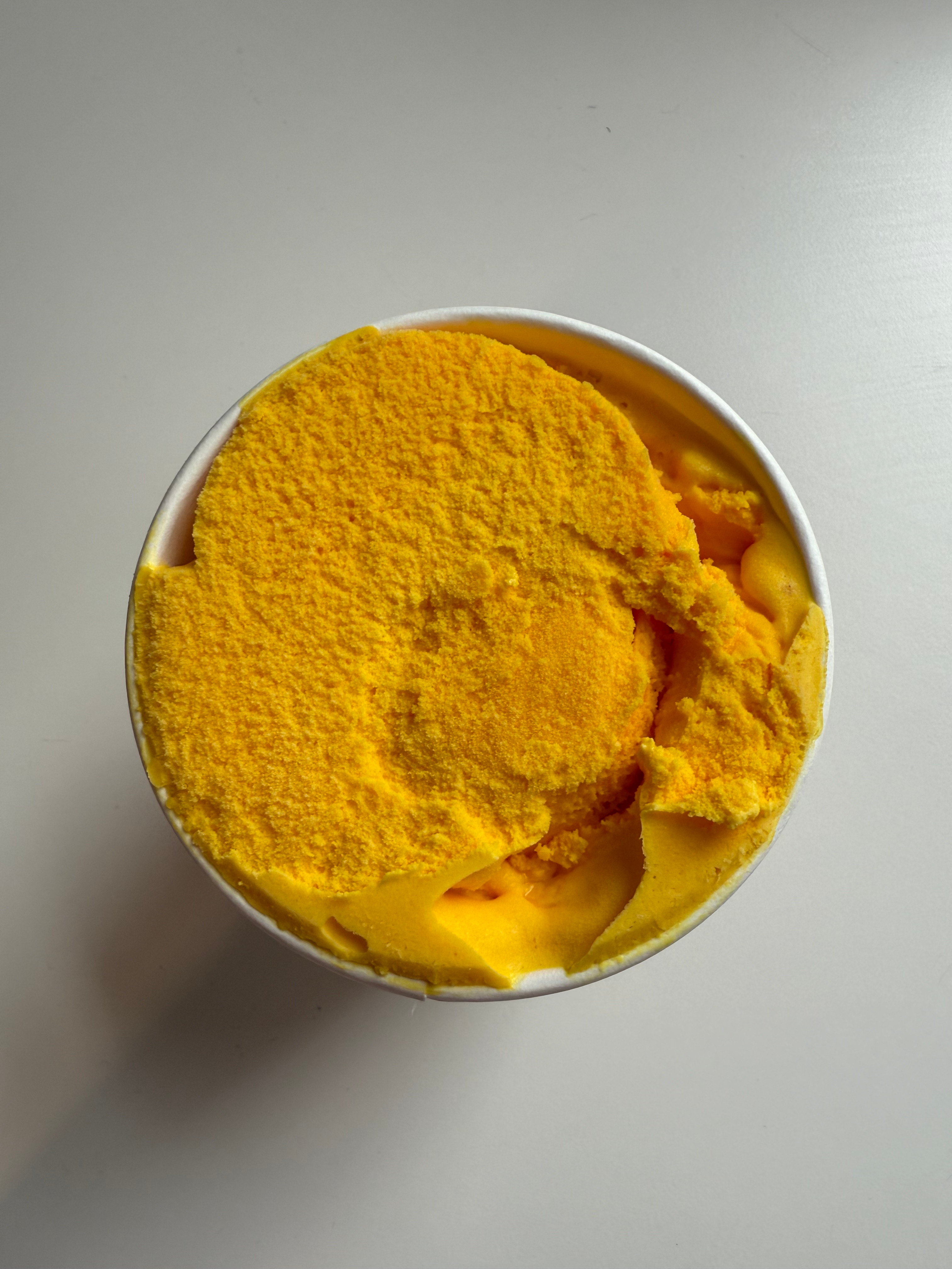 A tub of bright yellow ice cream with a smooth, slightly uneven surface, viewed from above