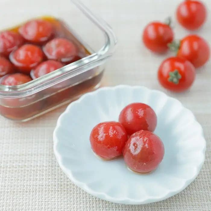 白い皿に盛られたミニトマトの前菜。背景には容器に入った他のトマトと余分なトマトが見える。