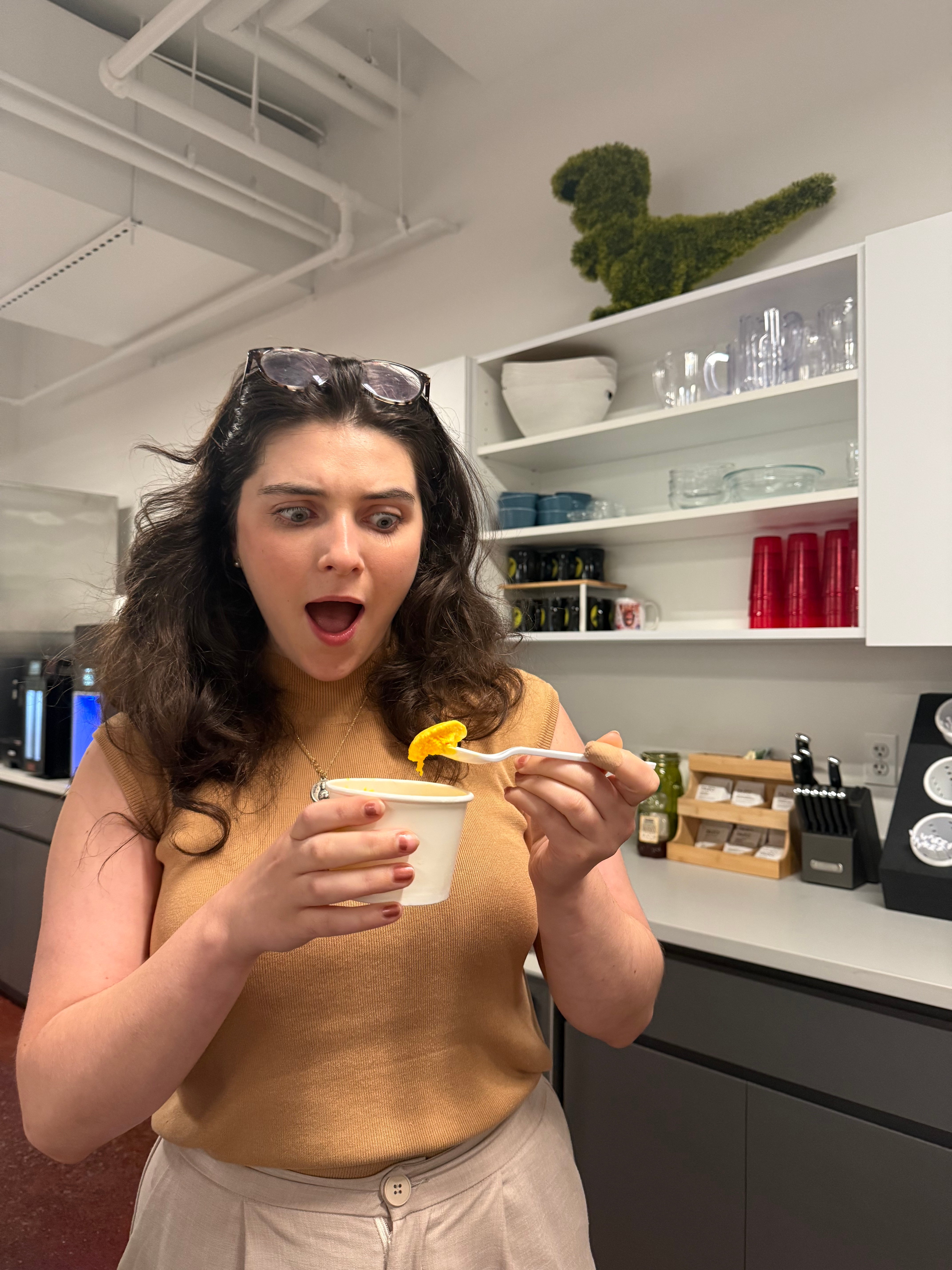 A surprised woman in a kitchen holds a spoon over a container, reacting to the food