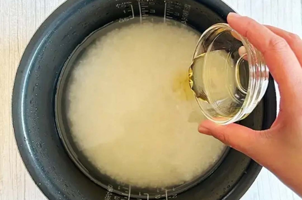 炊飯器の内釜に水が入った米。手が小さなガラス容器から液体を注いでいる。