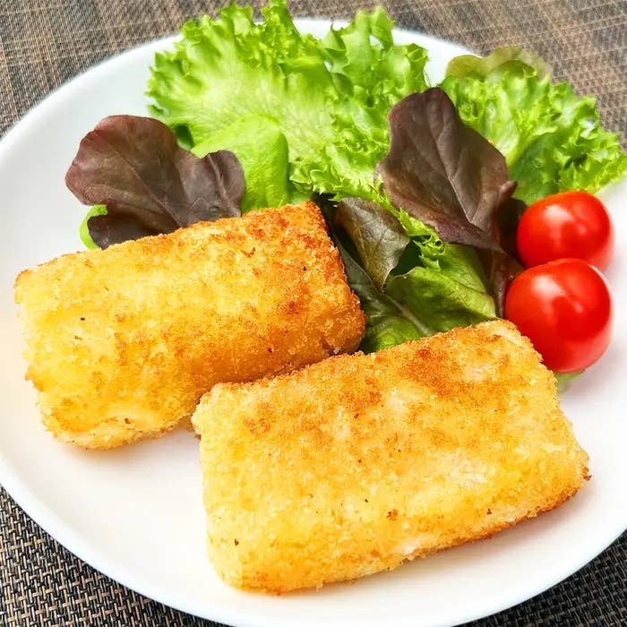 白い皿に盛られたカリッと揚げられた2つのライスペーパーでコーンクリームコロッケと、サニーレタス、ミニトマトが添えられています。