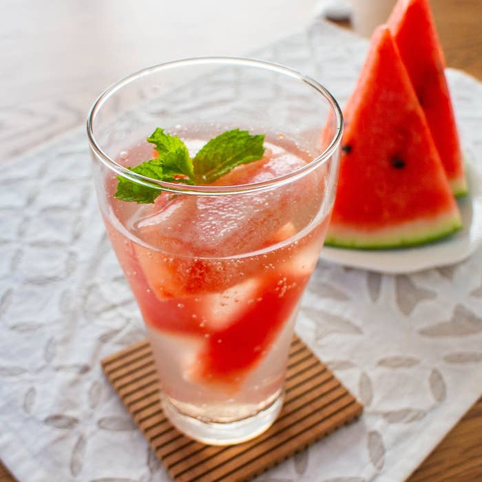 テーブルに置かれたスイカとミント入りの冷たい飲み物。後ろにスライスされたスイカが添えられている。