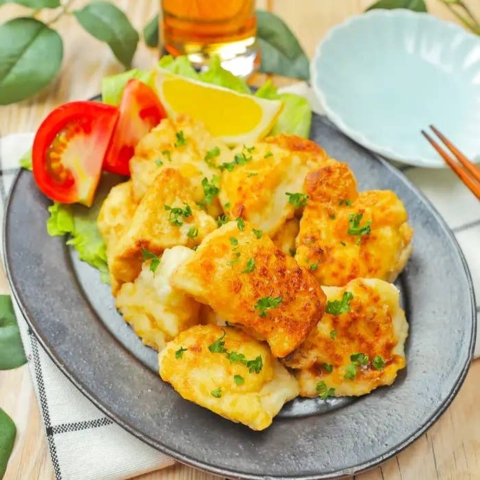 お皿に盛られた揚げた魚のフライ、トマトとレモンのスライス添え。後ろに飲み物のグラスと箸。