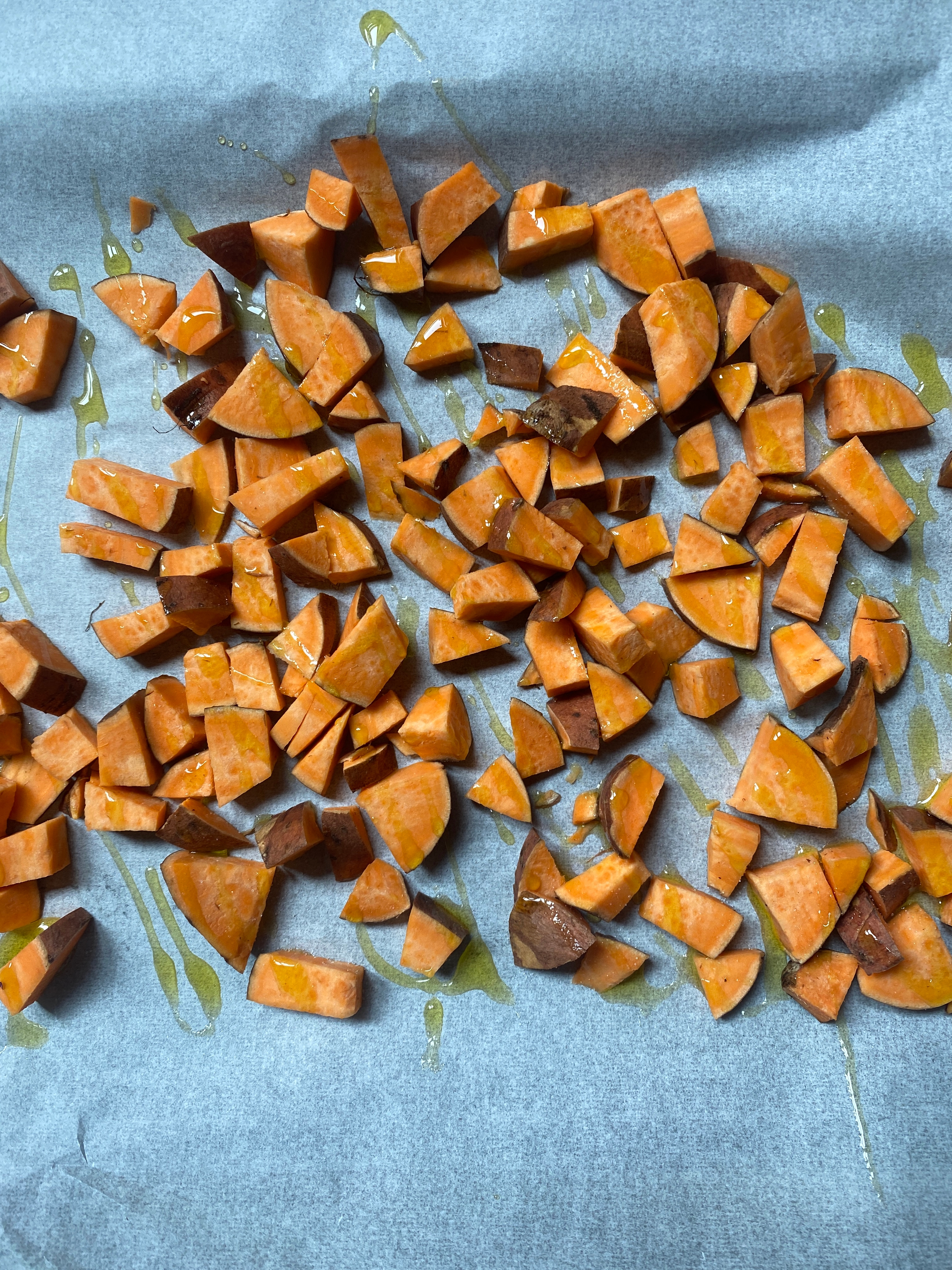 Chopped sweet potatoes on a baking sheet with drizzled oil, ready for roasting