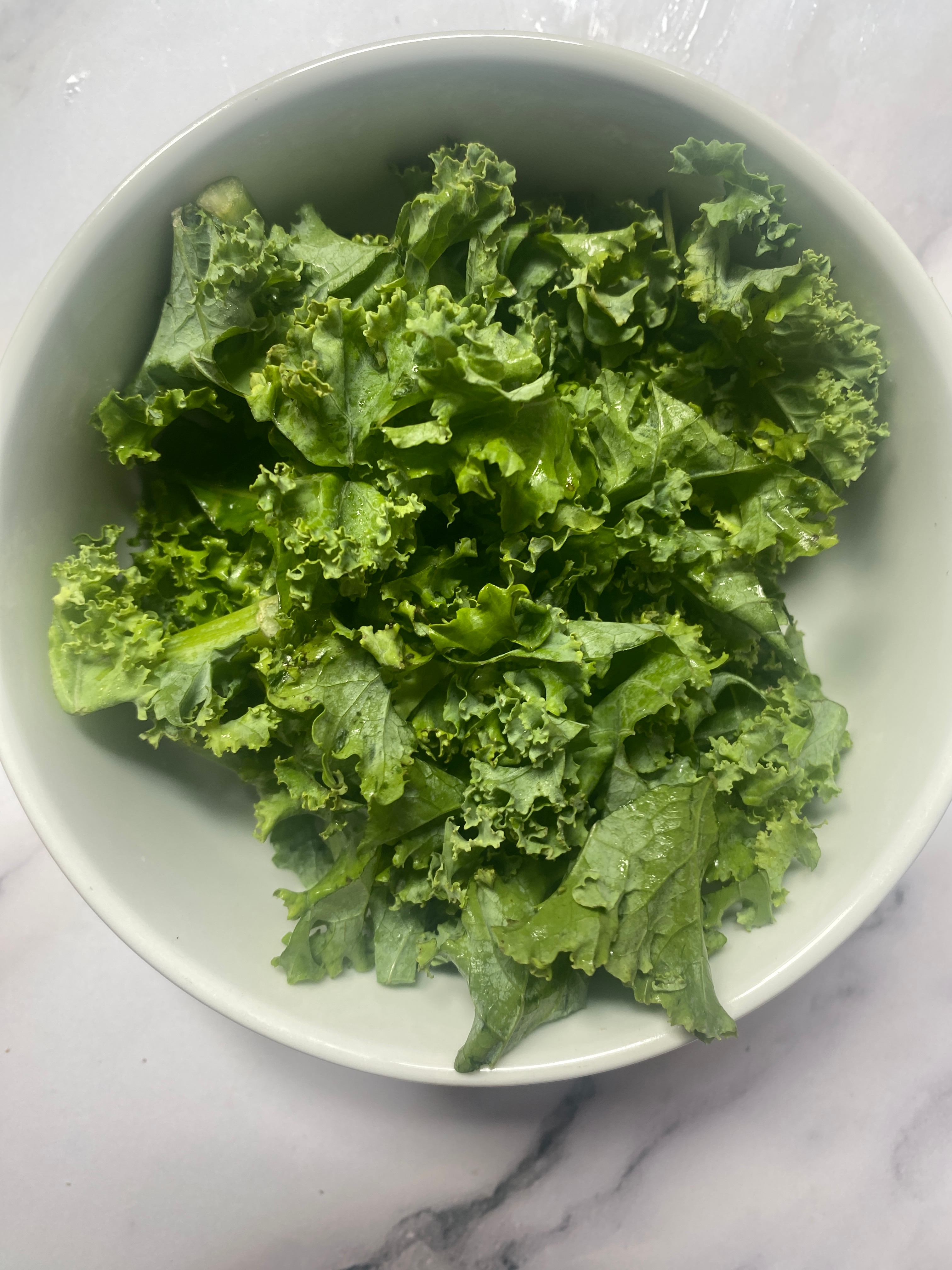 A bowl of fresh kale leaves on a marble surface