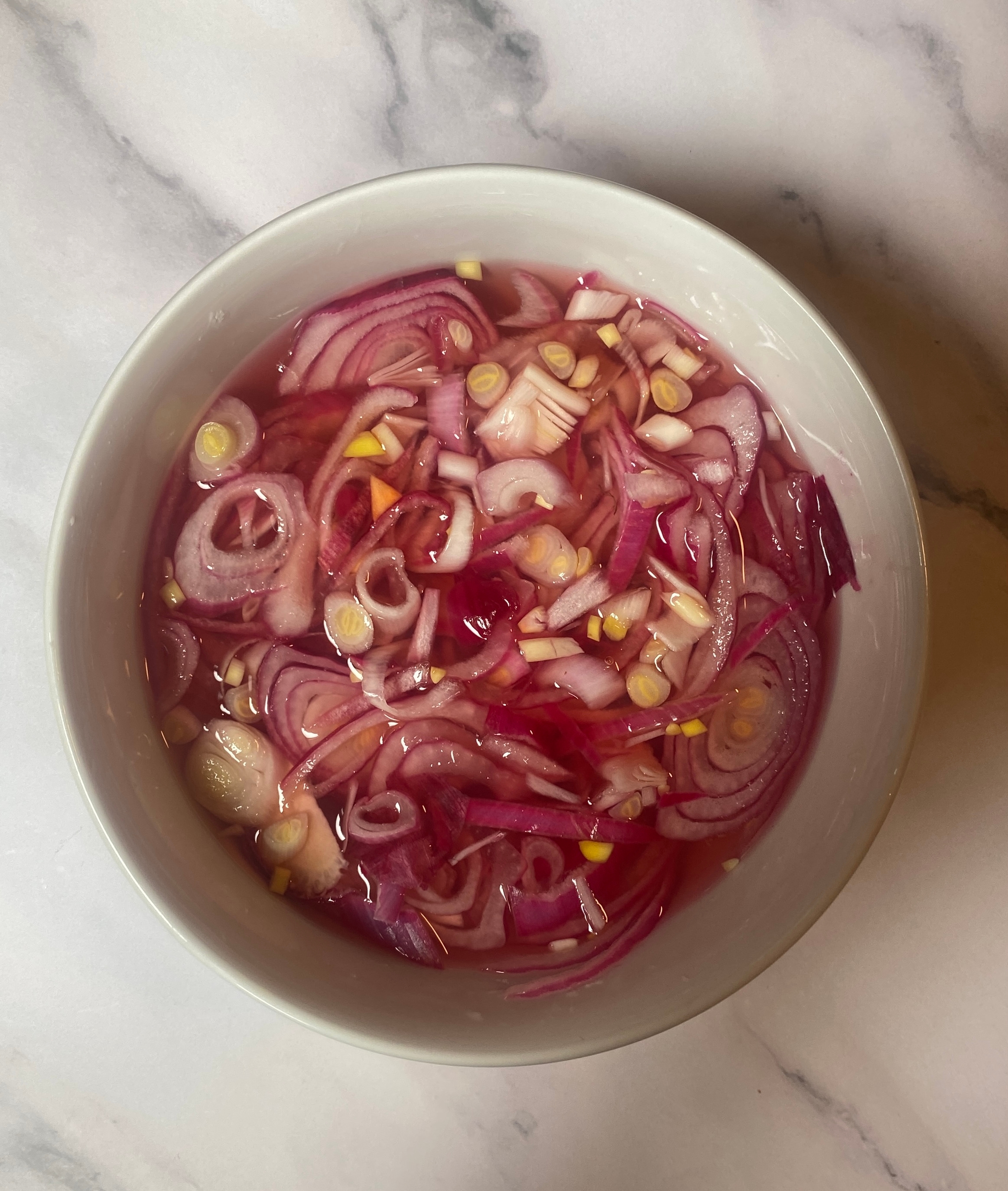 Bowl of sliced onions soaking in liquid, placed on a marble surface