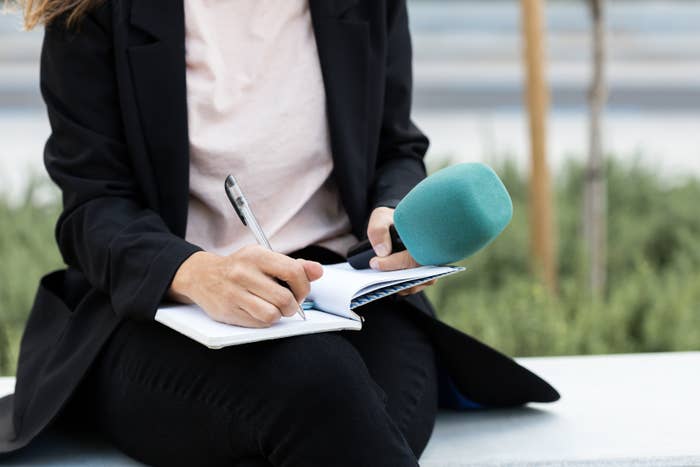 Person successful a achromatic blazer takes notes successful a notebook portion holding a microphone outdoors