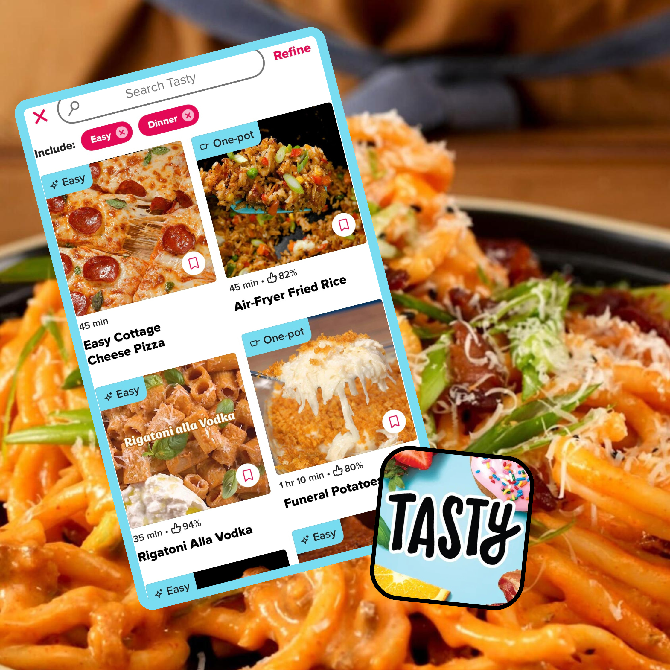 Close-up of a pasta dish behind a smartphone screen displaying various easy and one-pot meal options on the Tasty app, including pizza and fried rice