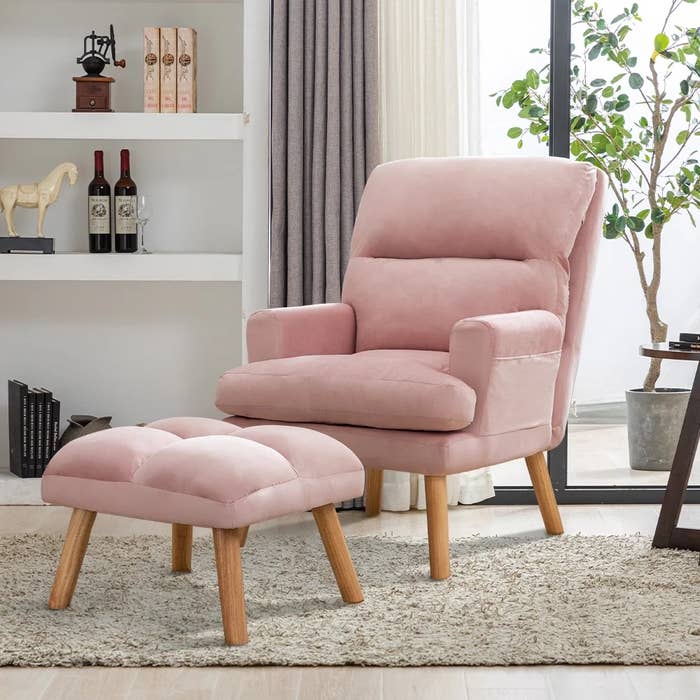 Plush armchair and footstool with woody legs successful a cozy surviving room, adjacent a window. Books, vino bottles, and decor connected support successful the background