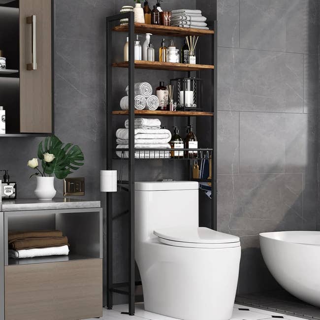 Bathroom with modern shelving implicit toilet, holding towels, toiletries, and decor. Minimalist plan with a freestanding tub and grey tiled walls