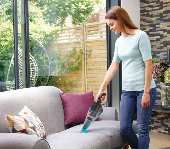 Person utilizing a handheld vacuum cleaner connected a sofa successful a modern surviving country with ample windows