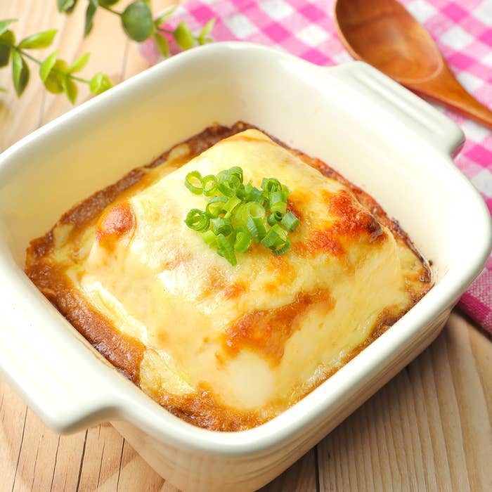 焼けたチーズがトッピングされたオニオングラタンスープが白い陶器の器に盛られている。青ネギが飾られている。