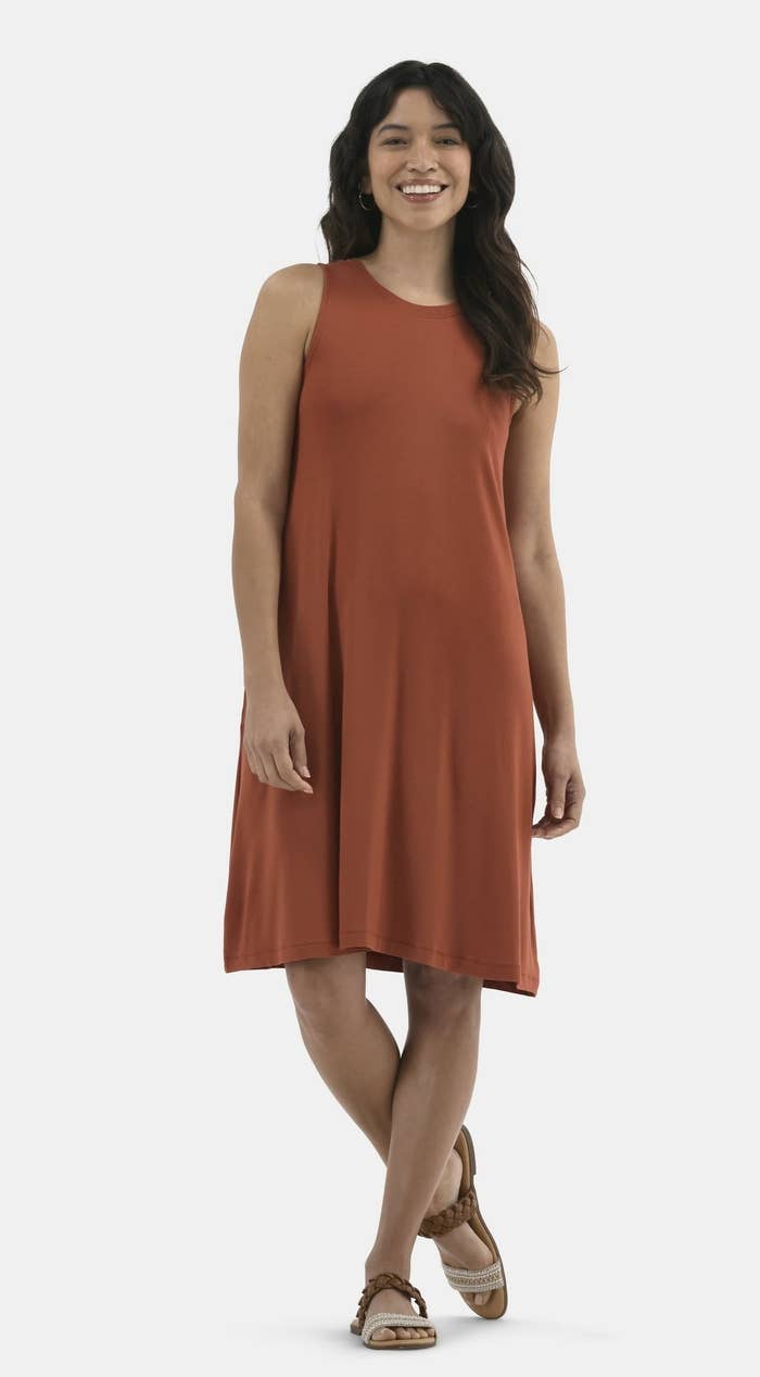 Model successful a sleeveless, knee-length formal with a relaxed fit, smiling and lasting casually