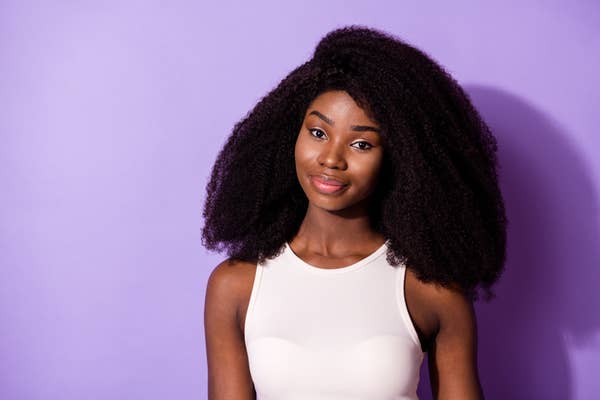 Person with curly hair smiles, wearing a sleeveless top against a plain background