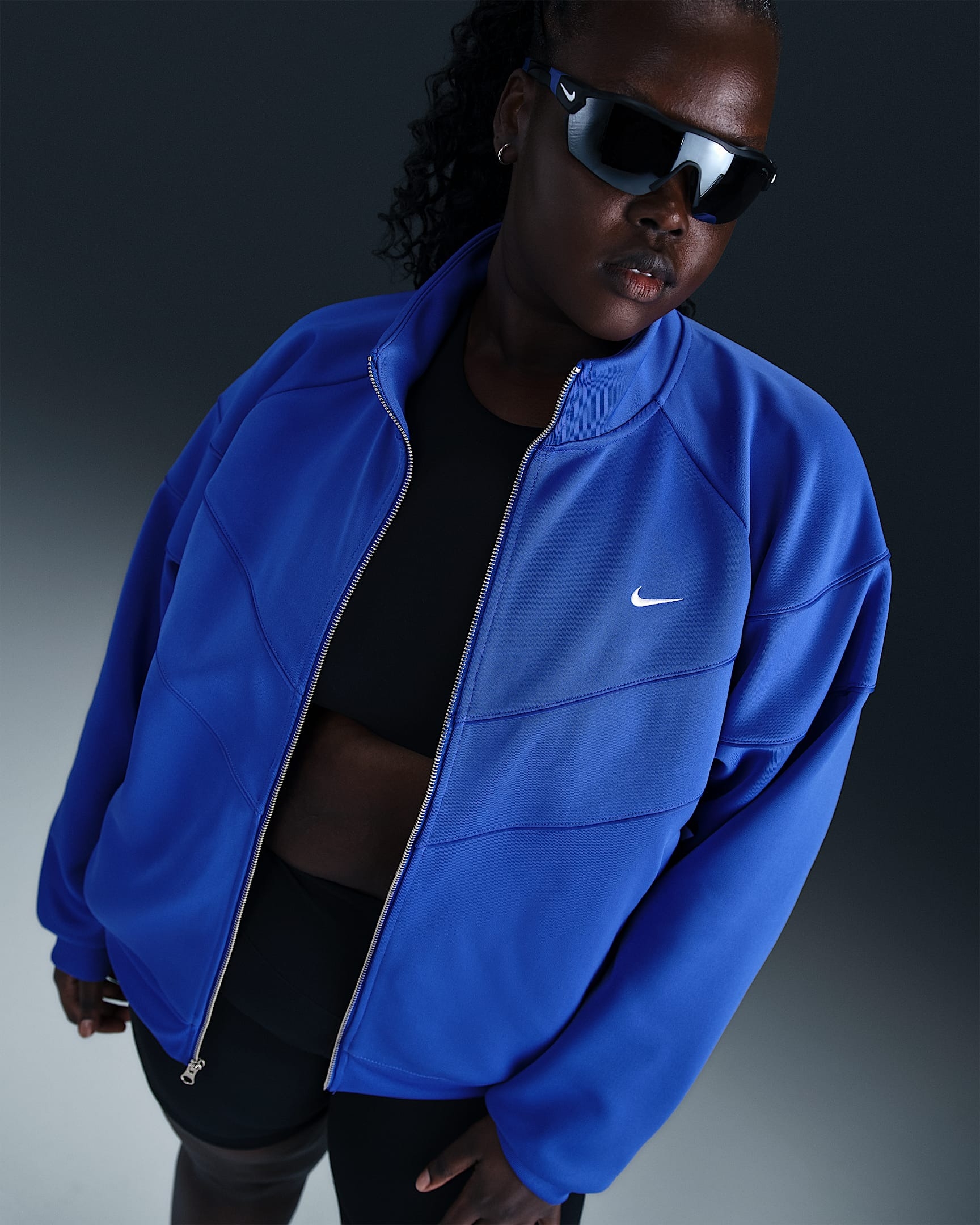 Person wearing a sporty blue Nike jacket, black top, shorts, and sunglasses, posing confidently in a shopping-related context