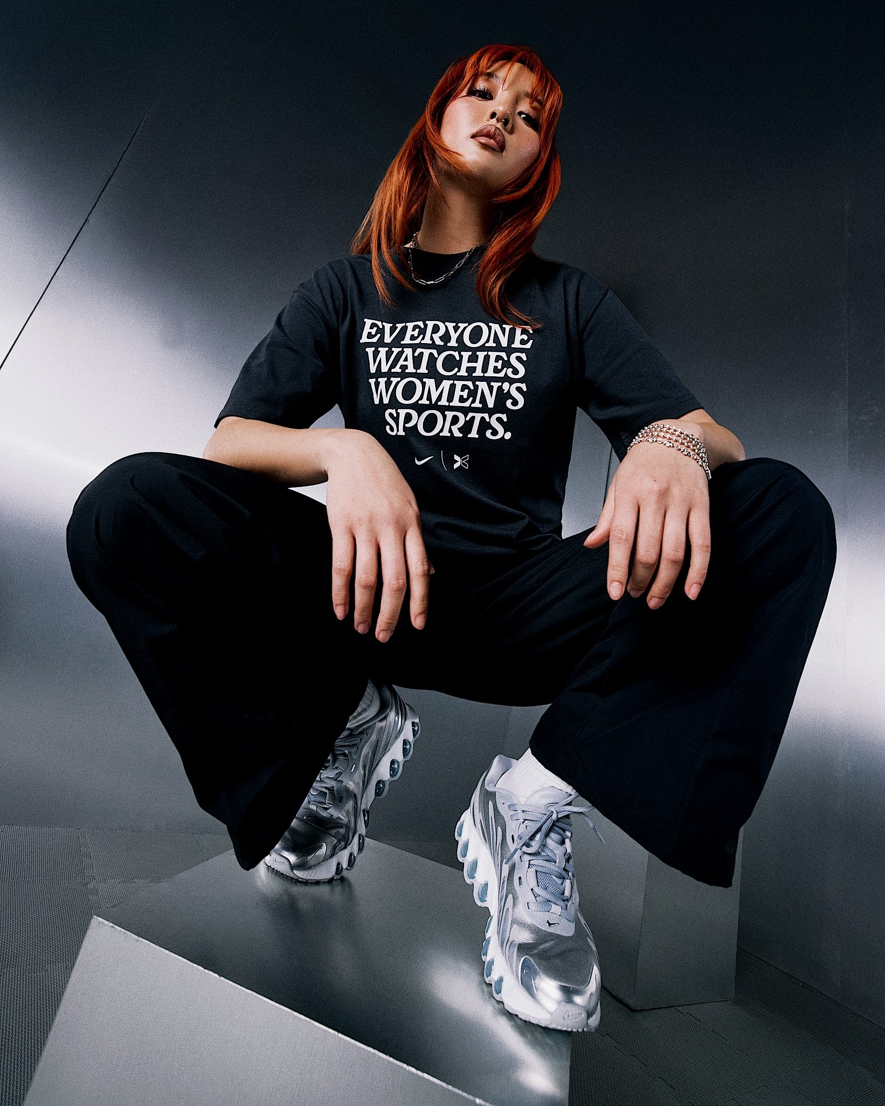 Person posing confidently, wearing a shirt with the text "Everyone watches women's sports," black pants, and sneakers, featured in a shopping article