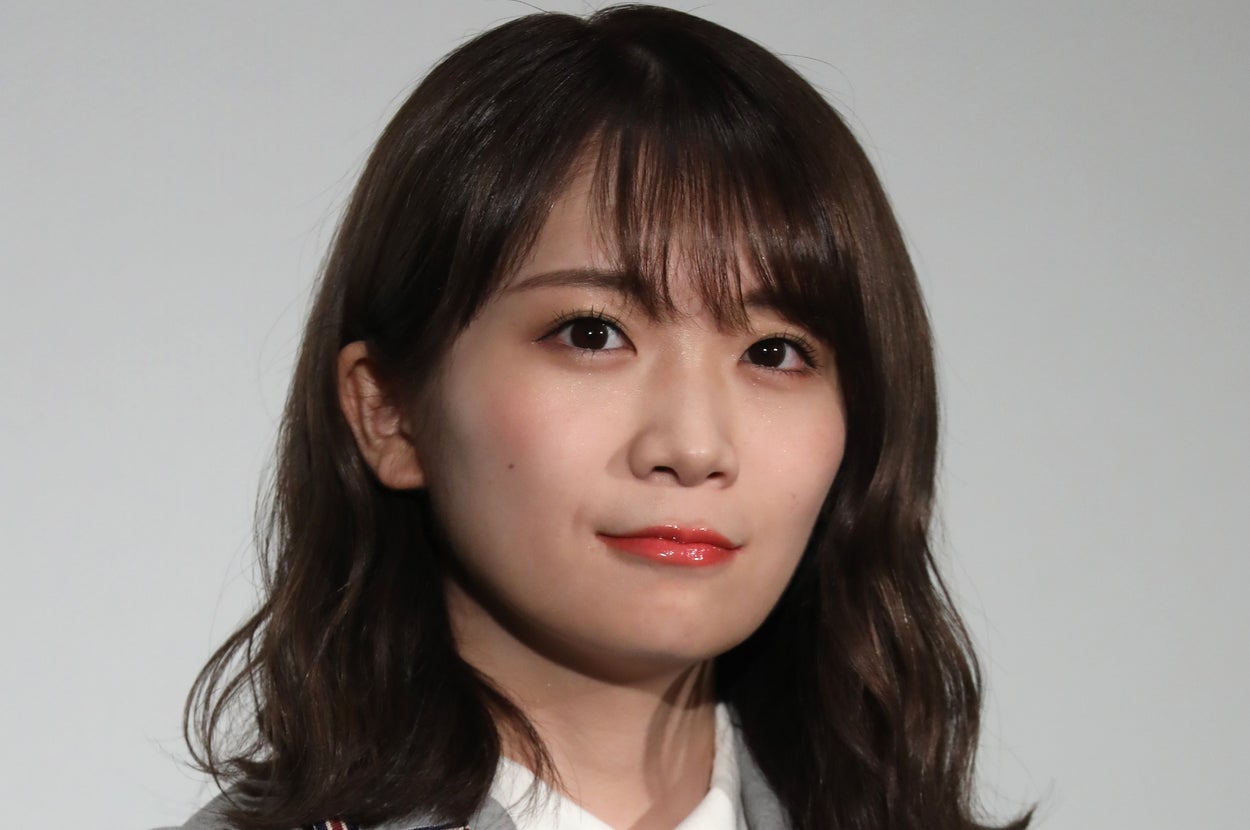 女性がステージでマイクを持ち、フォーマルなジャケットを着て立っている。