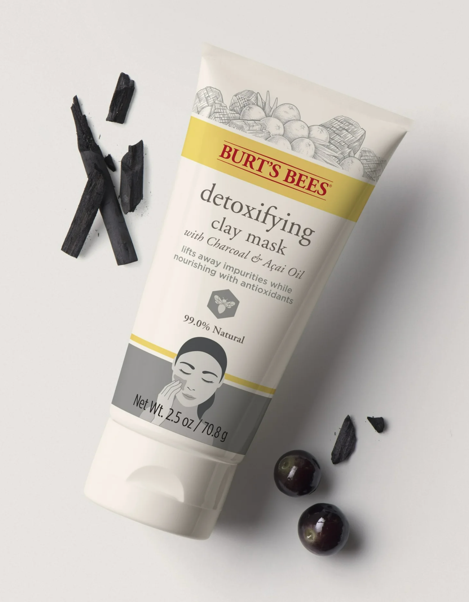 Burt's Bees Detoxifying Clay Mask tube with charcoal pieces and fruit details on a white background.