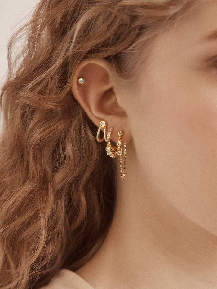 Person with golden earrings, including hoops and a chain, styled connected their ear.