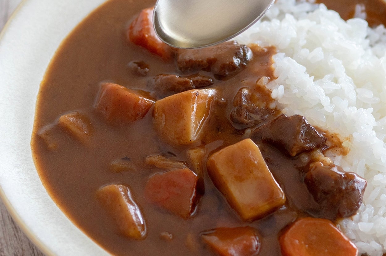 皿に盛られたカレーライス。スプーンが手前に見える。カレーには肉と野菜が入っている。