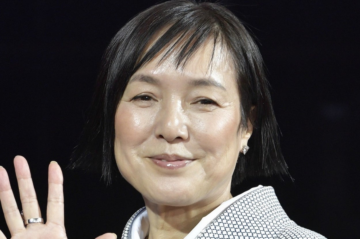 女性が伝統的な和服を着て微笑みながら手を振っています。