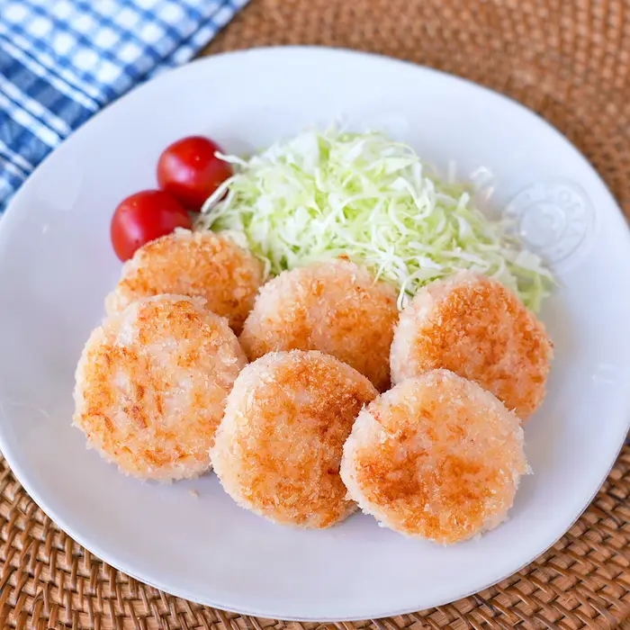 お皿に盛られたパン粉を使った白身魚フライ、千切りキャベツ、ミニトマトの食事。