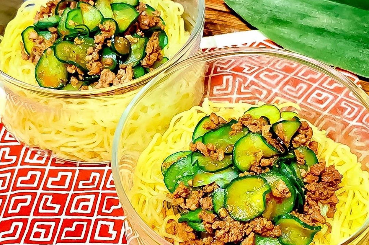 透明なガラスの器に麺とキュウリ、挽き肉が盛られた2つの料理。赤いパターンのクロスの上に置かれている。