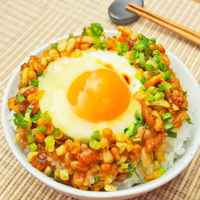 ご飯の上に目玉焼きと炒めたネギとカリカリのトッピングがのった料理。箸が横に置かれる。