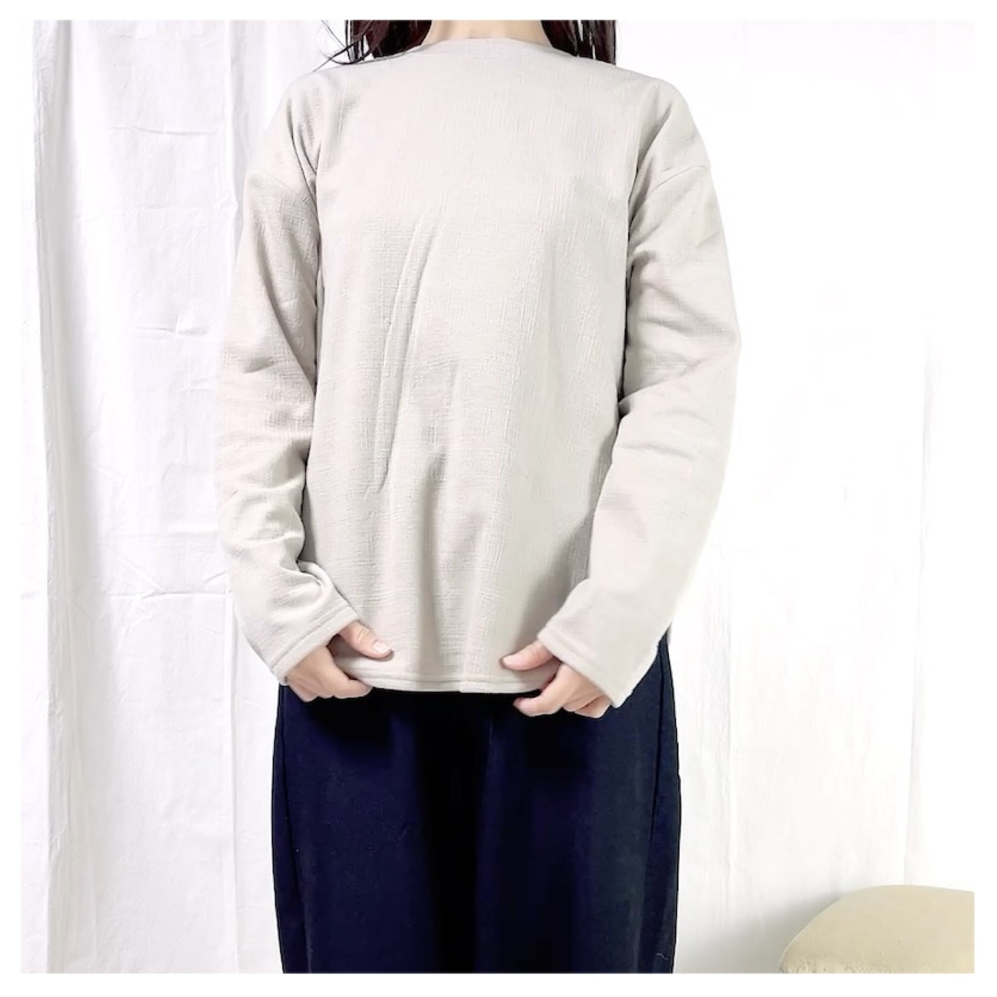 ゆったりとした長袖シャツとパンツを着た立っている人。顔は見えていない。シンプルなカジュアルファッション。