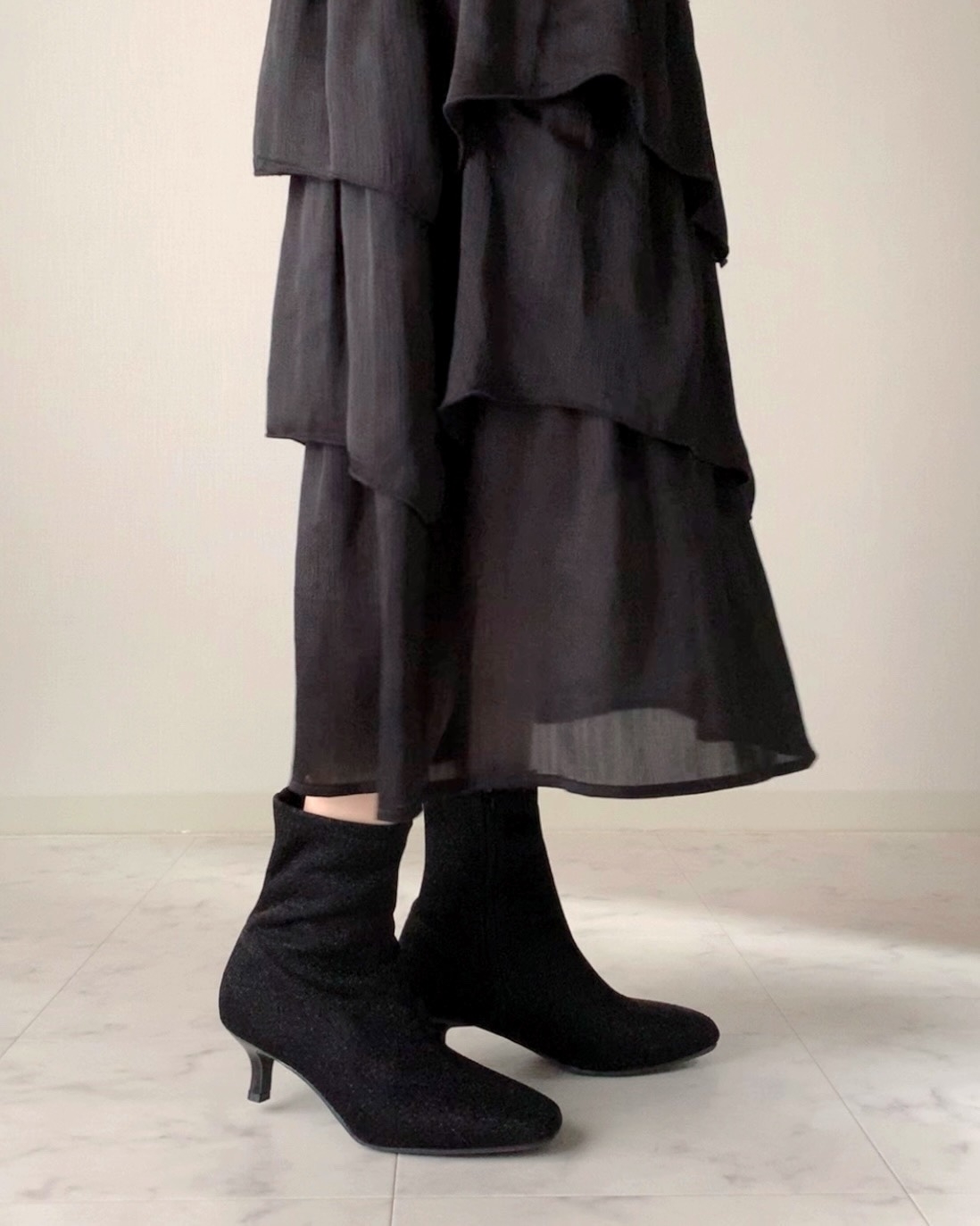 短い階段状のフリルの黒いドレスとヒールのあるブーツを履いた人物の下半身。
