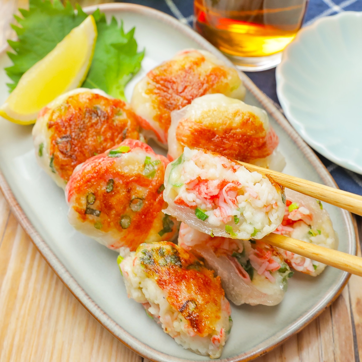 皿に盛られた美味しそうな焼き餃子。箸で持ち上げられた餃子の断面には具材が詰まっている。背景に飲み物。