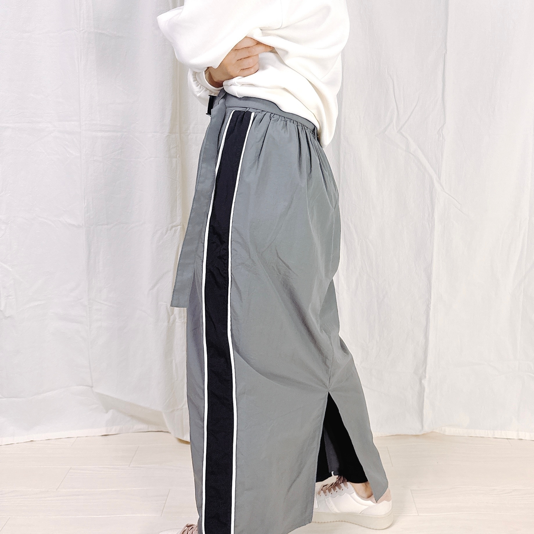 白いトップスとグレーのスカートを着た人が横向きで立っている。