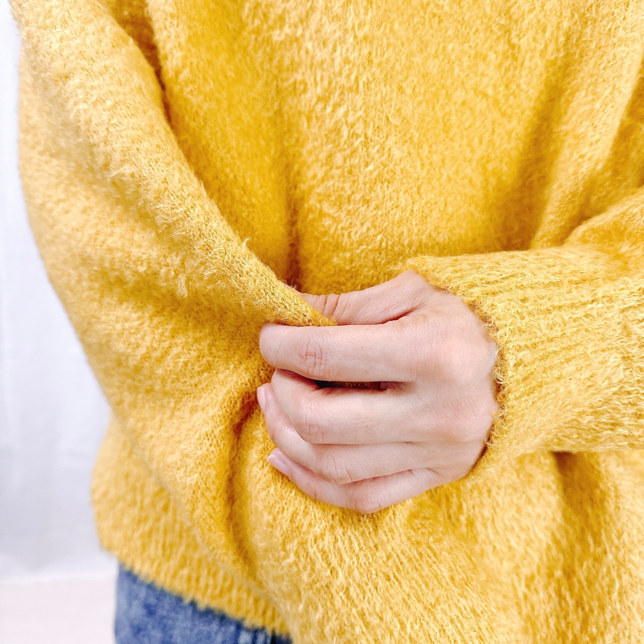 手編みのセーターを着た人が、その袖を軽く掴んでいる手元の様子。