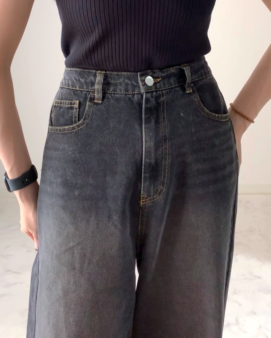 黒のノースリーブトップスとデニムを着た女性の上半身が映った写真。
