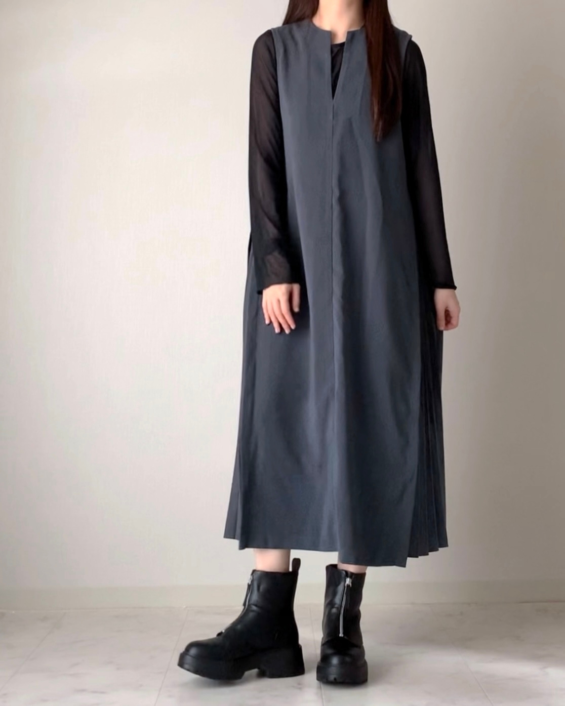 女性が丈の長いシンプルなノースリーブドレスを着て、足元はブーツを履いている。顔は写っていない。