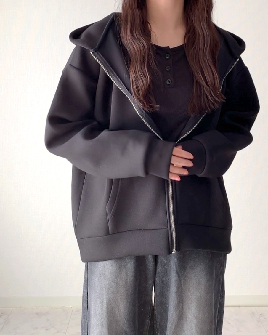 ゆったりとした黒いジップアップパーカーとワイドなパンツを着た人物の上半身。顔は見えない。