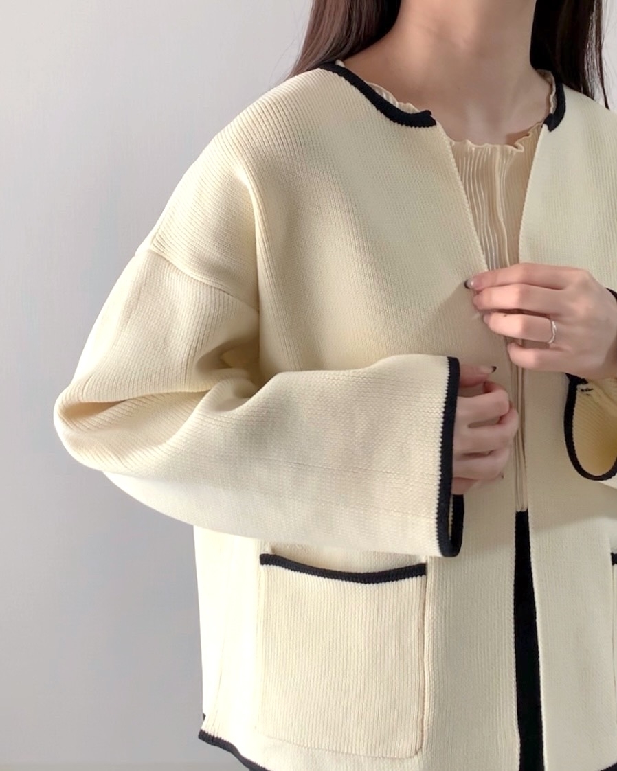 女性が縁取りが施されたカーディガンを着て前を止めている。
