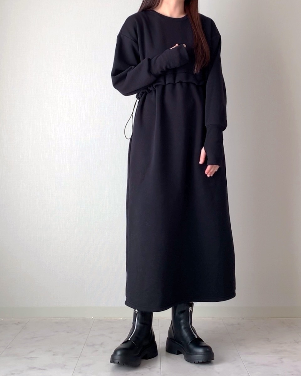 女性が長袖のシンプルなロングワンピースとブーツを着用。顔は写っていない。